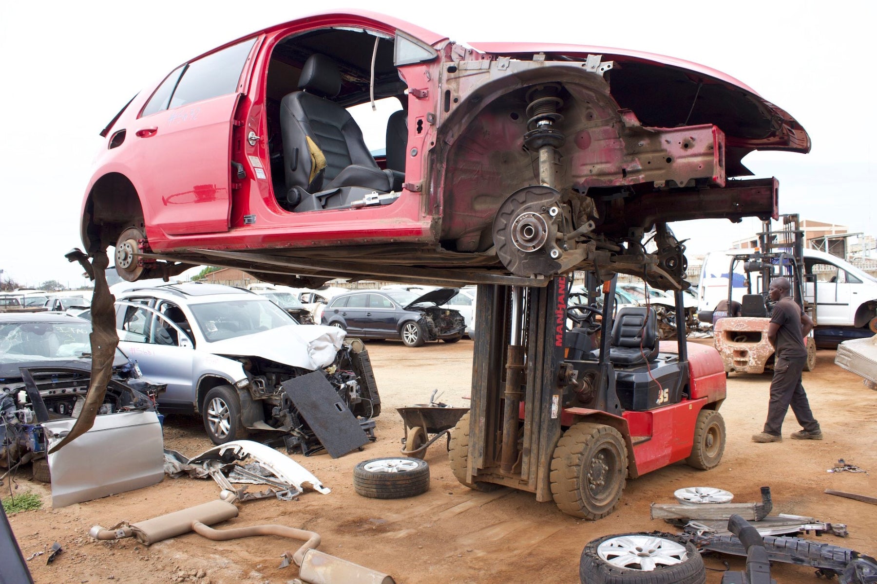 Red car on a forklift in a junkyard setting