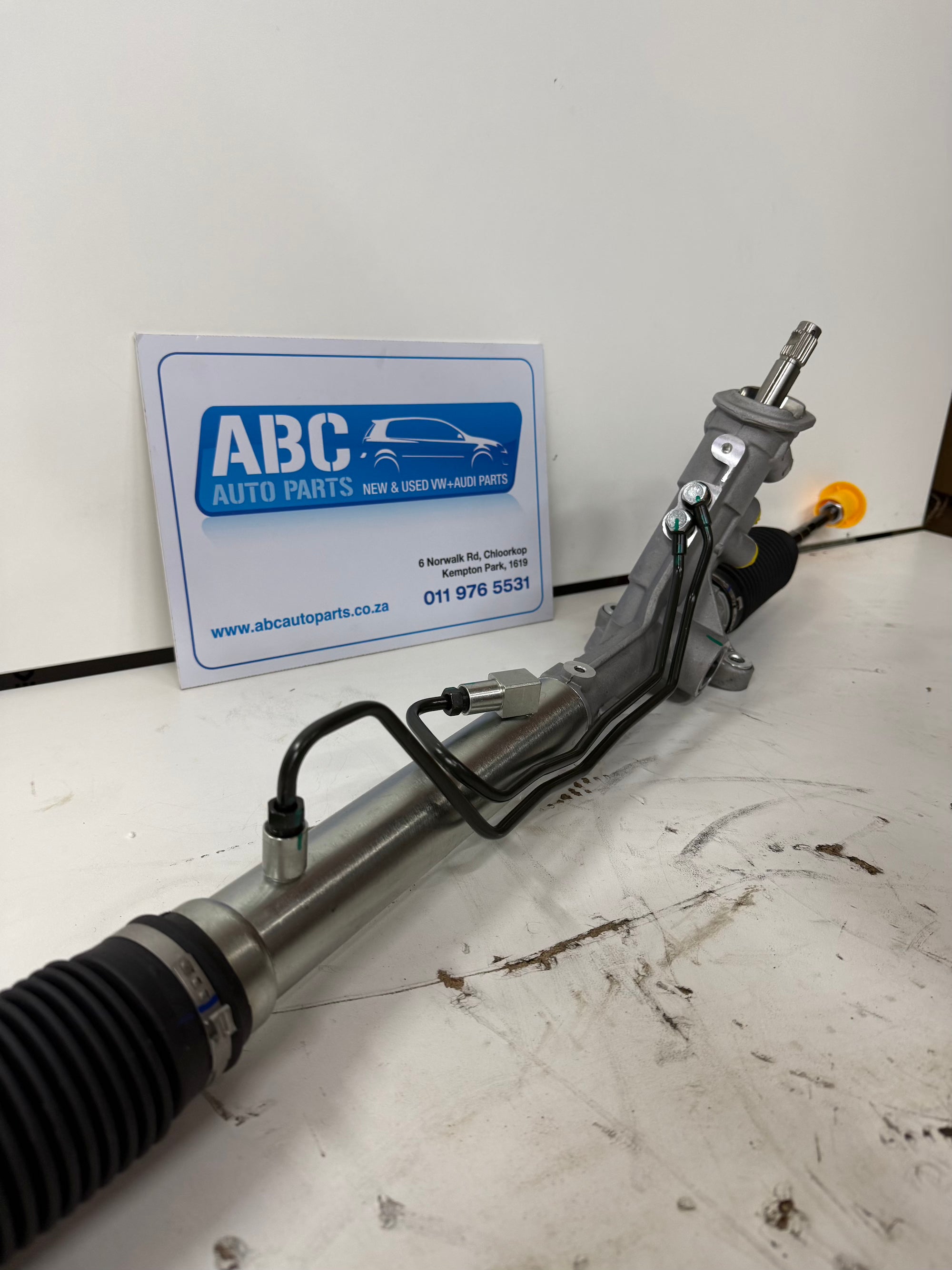 Car steering rack on a white surface with ABC Auto Parts sign in the background